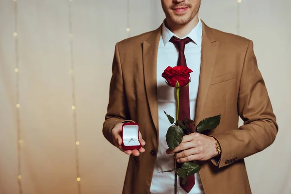 Partial view of elegant man holding box with wedding ring and red rose while standing in restaurant — Stock Photo