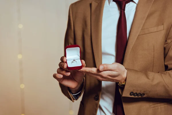 Cropped view of elegant man showing box with wedding ring while standing in restaurant — Stock Photo