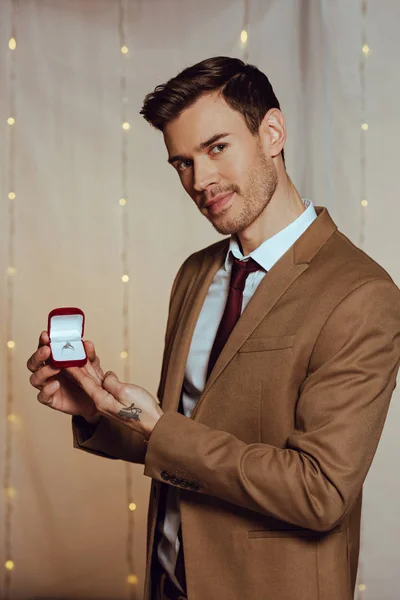 Elegante, bonito homem segurando caixa com anel de casamento enquanto olha para a câmera — Fotografia de Stock