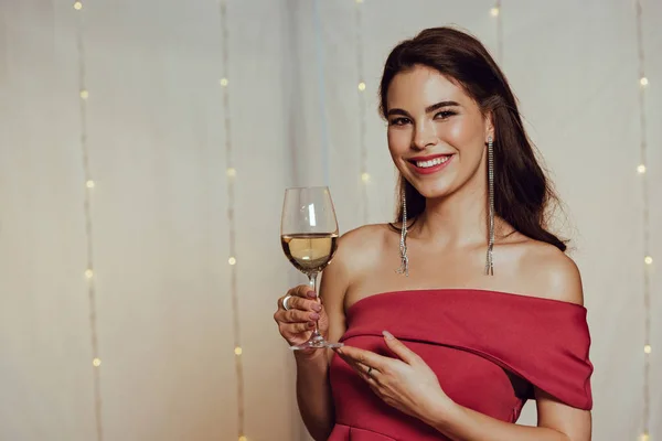 Menina feliz e elegante sorrindo para a câmera enquanto segurando um copo de vinho branco no restaurante — Fotografia de Stock