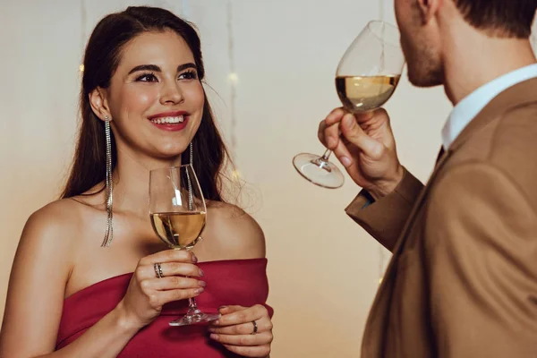 Foco seletivo de atraente, menina feliz olhando para o namorado enquanto segurando copo de vinho branco — Fotografia de Stock