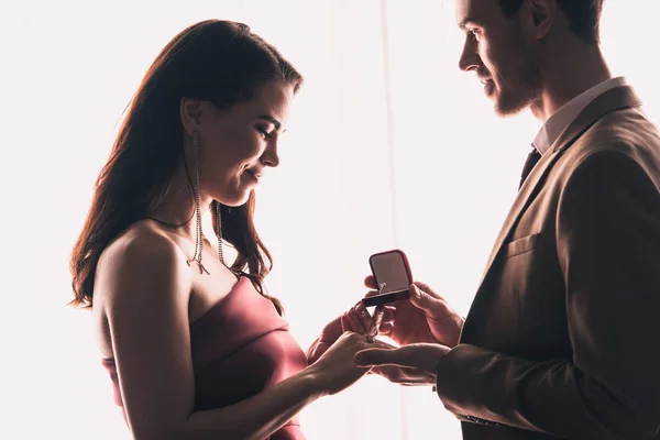 Vista lateral del hombre guapo presentando anillo a novia feliz mientras que hace propuesta de matrimonio en San Valentín - foto de stock