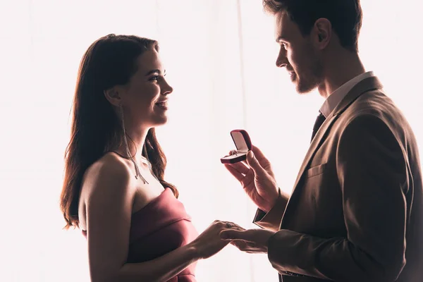 Seitenansicht eines gutaussehenden Mannes, der die Hand einer glücklichen Freundin hält, während er einen Heiratsantrag an Valentinstagen macht — Stockfoto