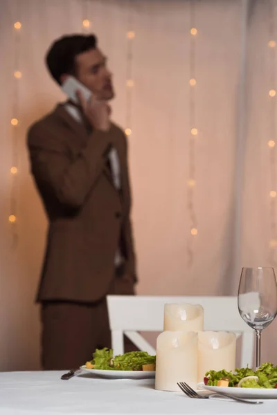 Selective focus of elegant man talking on smartphone while standing near served table in restaurant — Stock Photo