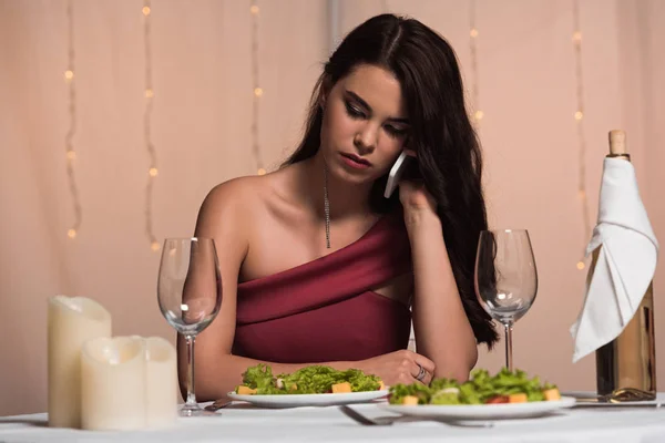 Menina desapontada, elegante sentado à mesa servida no restaurante e falando no smartphone — Fotografia de Stock