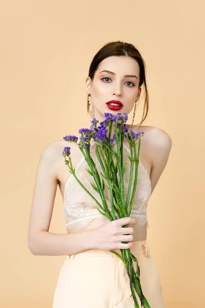 Hermosa mujer sosteniendo flores púrpuras aisladas en beige - foto de stock