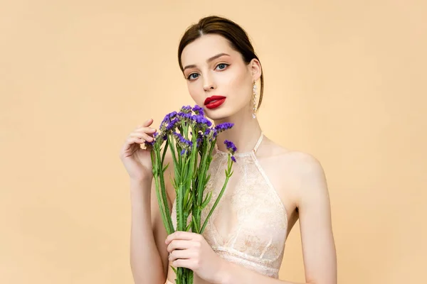 Giovane bella donna che tiene fiori di limonio viola isolati su beige — Foto stock