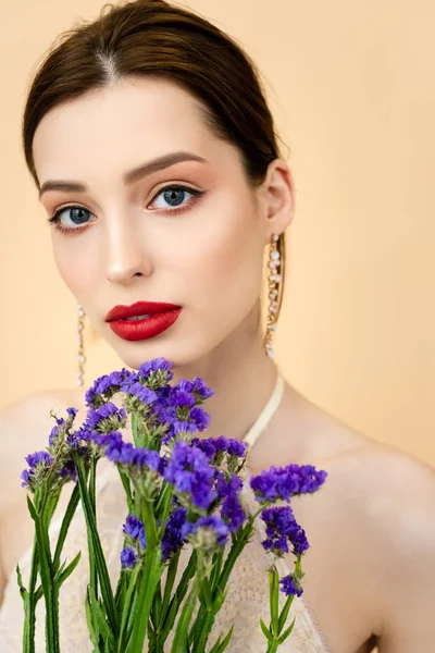 Hermosa mujer mirando a la cámara cerca de flores de limonio púrpura aislado en beige - foto de stock