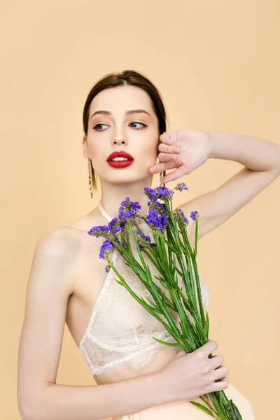 Beautiful woman looking away and holding purple limonium flowers isolated on beige — Stock Photo