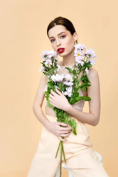 Belle femme aux lèvres rouges tenant des fleurs fleuries isolées sur beige — Photo de stock
