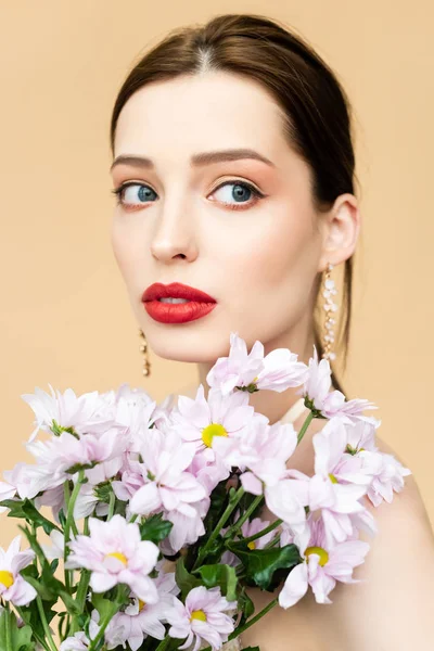 Chica bonita mirando hacia otro lado cerca de flores de crisantemo aisladas en beige - foto de stock