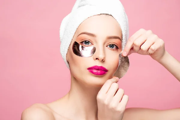Bella giovane donna in asciugamano applicare macchie oculari isolate su rosa — Foto stock