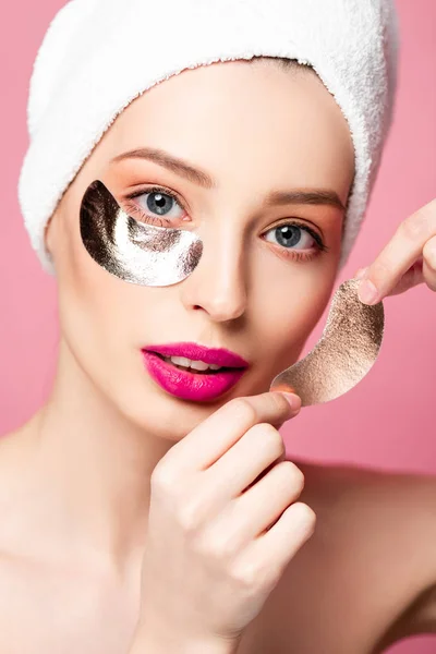 Bela mulher em enquanto toalha aplicando manchas oculares isoladas em rosa — Fotografia de Stock