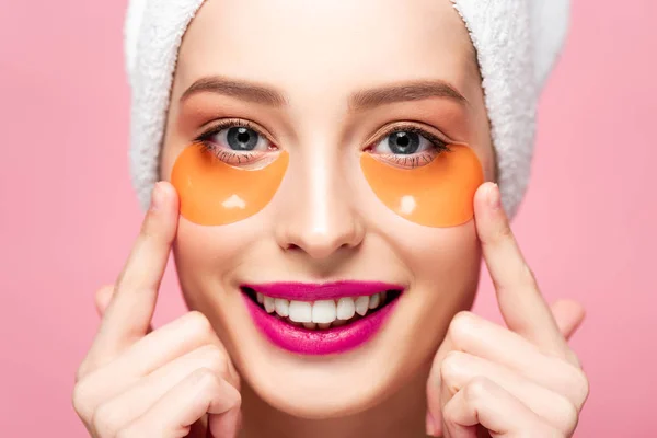 Smiling girl touching face with eye patches isolated on pink — Stock Photo