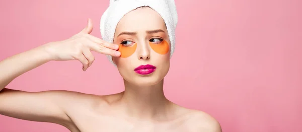 Plan panoramique de fille nue touchant le visage avec des patchs pour les yeux isolés sur rose — Photo de stock