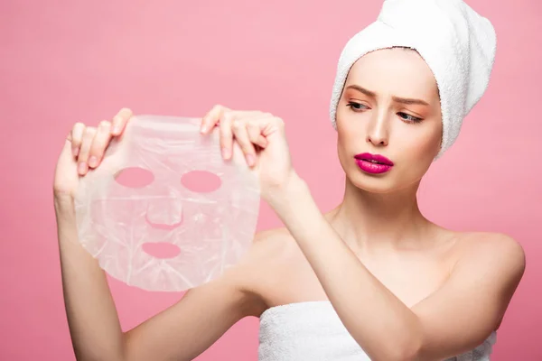 Hübsches Mädchen mit Blick auf feuchtigkeitsspendende Gesichtsmaske isoliert auf rosa — Stockfoto