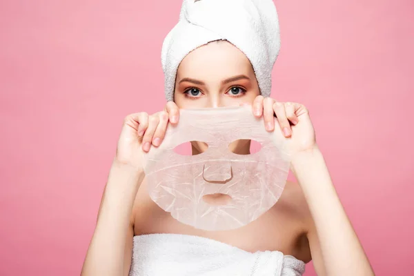 Mujer joven cubriendo la cara mientras sostiene mascarilla hidratante aislado en rosa - foto de stock
