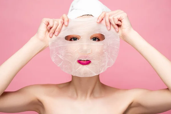 Joven mujer desnuda cubriendo la cara mientras se aplica mascarilla hidratante aislado en rosa - foto de stock