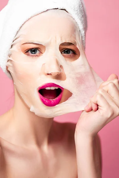 Scioccato giovane donna toccando maschera isolata su rosa — Foto stock