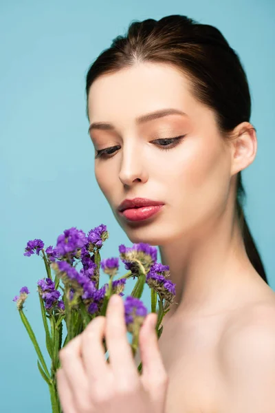 Foco seletivo de mulher nua perto de flores de limonium isolado em azul — Fotografia de Stock