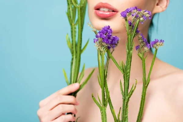 Vista recortada de chica desnuda sosteniendo flores de limonio aisladas en azul - foto de stock