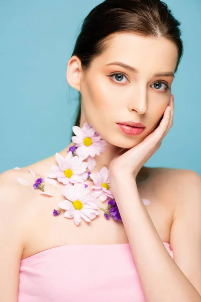 Junge Frau mit Blumen am Hals blickt vereinzelt in die Kamera auf blauem Grund — Stockfoto