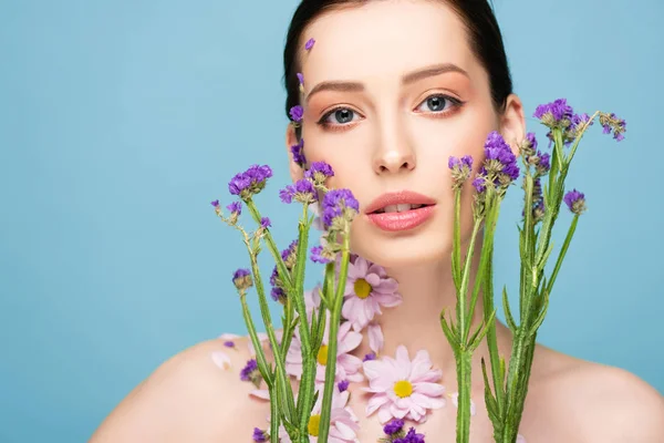 Attractive and naked woman near blooming flowers isolated on blue — Stock Photo