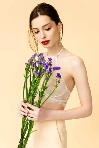 Mulher atraente olhando para flores de limonium roxo isolado no bege — Fotografia de Stock