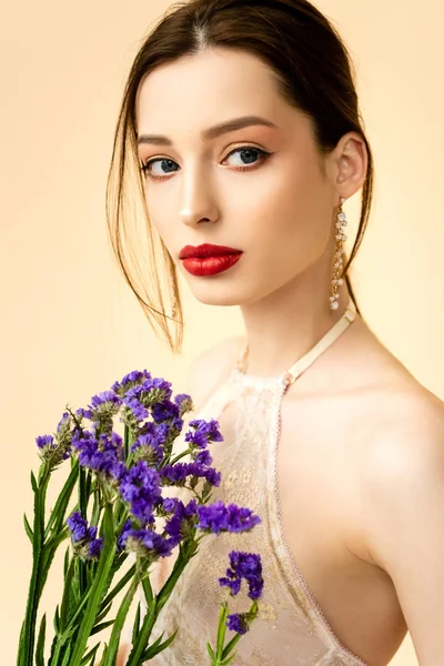 Mujer atractiva joven sosteniendo flores de limonio aisladas en beige - foto de stock