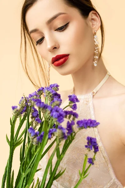 Jovem e atraente mulher segurando flores de limonium roxo isolado no bege — Fotografia de Stock