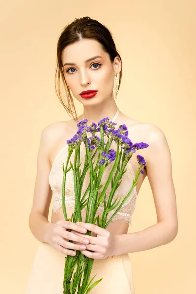 Jeune femme tenant des fleurs de limonium violet isolé sur beige — Photo de stock