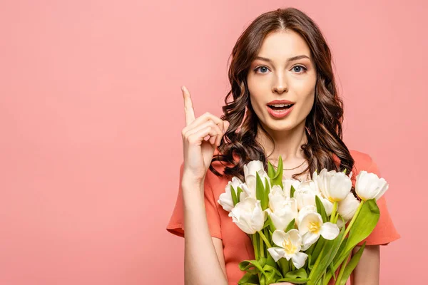 Attractive girl blowing showing idea gesture while holding bouquet of white tulips isolated on pink — Stock Photo