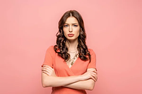 Scontento giovane donna in piedi con le braccia incrociate mentre guarda la fotocamera isolata su rosa — Foto stock