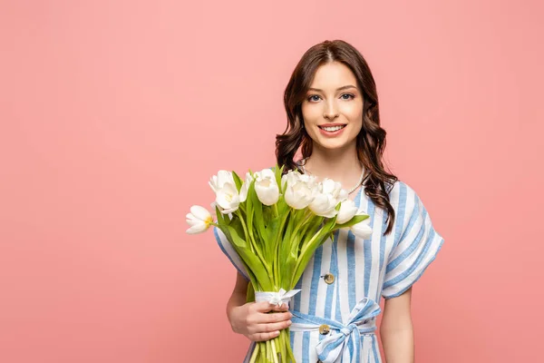 Cheerful girl smiling at camera while holding bouquet of white tulips isolated on pink — Stock Photo