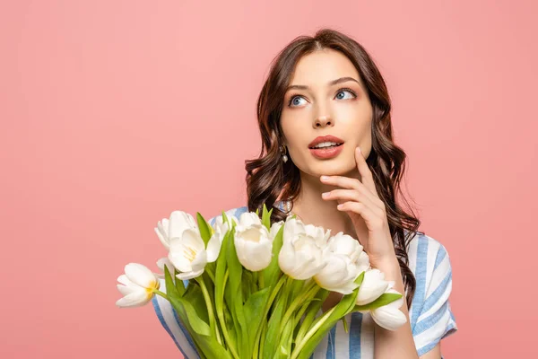 Verträumtes Mädchen schaut weg, während es einen Strauß weißer Tulpen in der Hand hält und die Wange berührt, isoliert auf rosa — Stockfoto
