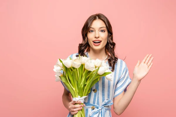 Aufgeregtes Mädchen winkt mit der Hand in die Kamera und hält einen Strauß weißer Tulpen auf rosa — Stockfoto