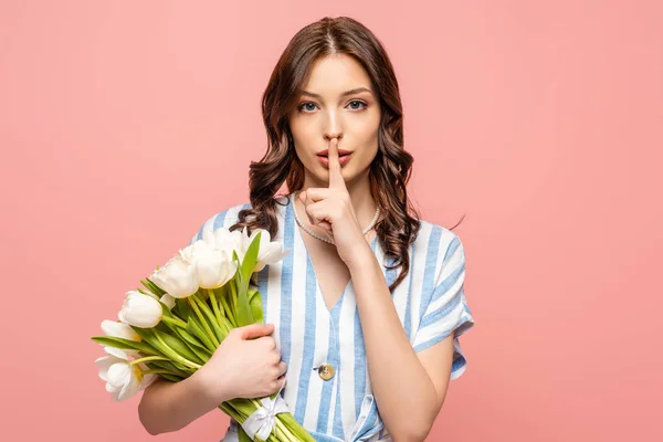 Serious girl showing hush sign while holding bouquet of white tulips isolated on pink — Stock Photo