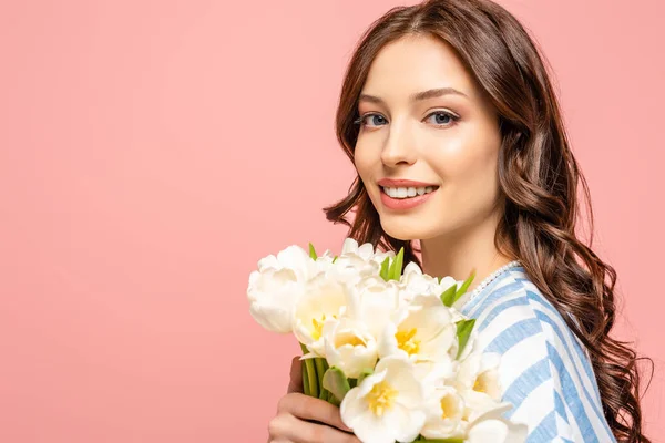 Happy girl holding bouquet of white tulips while smiling at camera isolated on pink — Stock Photo