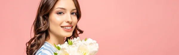 Plan panoramique de fille heureuse tenant bouquet de tulipes blanches et regardant la caméra isolée sur rose — Photo de stock