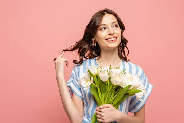 Glückliches Mädchen, das die Haare berührt, während es einen Strauß weißer Tulpen in der Hand hält und isoliert auf rosa — Stockfoto