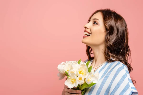 Щаслива дівчина, дивлячись вгору, тримає букет білих тюльпанів ізольовані на рожевому — стокове фото