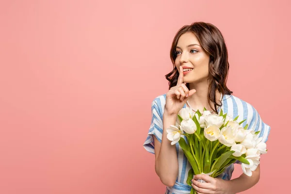 Attractive girl showing hush gesture while holding bouquet of white tulips isolated on pink — Stock Photo