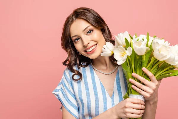 Chica feliz sonriendo a la cámara mientras sostiene ramo de tulipanes blancos aislados en rosa - foto de stock