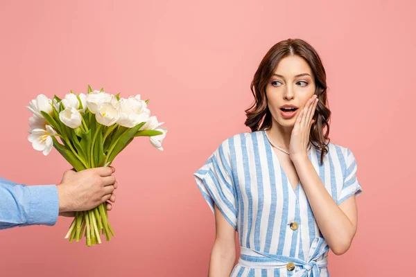 Partial view of man presenting bouquet of white tulips to surprised girl isolated on pink — Stock Photo