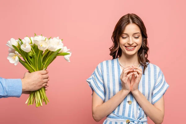 Vue partielle de l'homme présentant bouquet de tulipes blanches à fille heureuse debout avec les yeux fermés isolés sur rose — Photo de stock