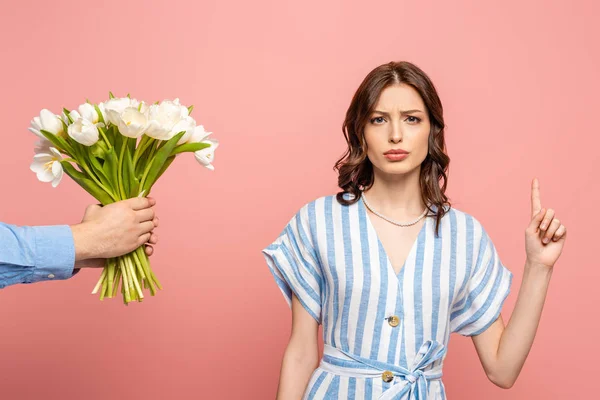 Partial view of man presenting bouquet of white tulips to serious girl showing idea gesture isolated on pink — Stock Photo