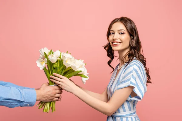 Cropped view of man presenting bouquet of white tulips to cheerful young woman isolated on pink — Stock Photo