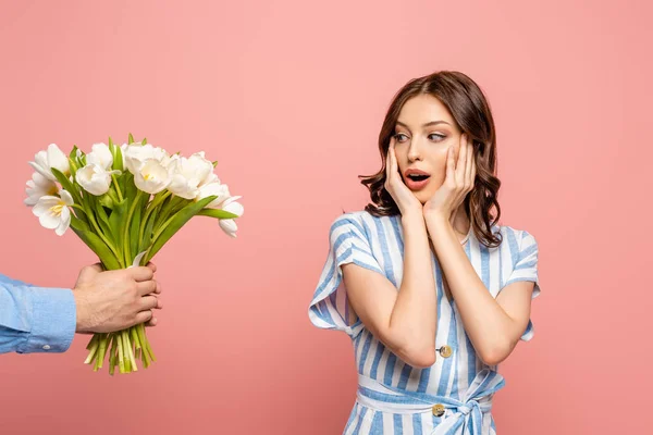 Cropped view of man presenting bouquet of white tulips to surprised young woman isolated on pink — Stock Photo