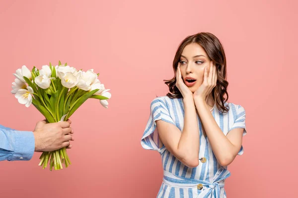 Vista ritagliata di uomo che presenta bouquet di tulipani bianchi a sorpresa giovane donna isolata su rosa — Foto stock