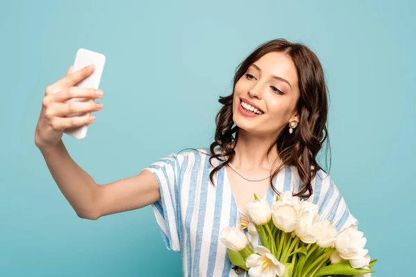 Feliz jovem mulher tomando selfie no smartphone enquanto segurando enquanto tulipas isoladas no azul — Fotografia de Stock